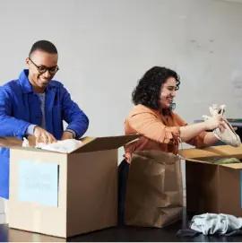 The image depicts two individuals engaged in an activity that involves packing or unpacking items.